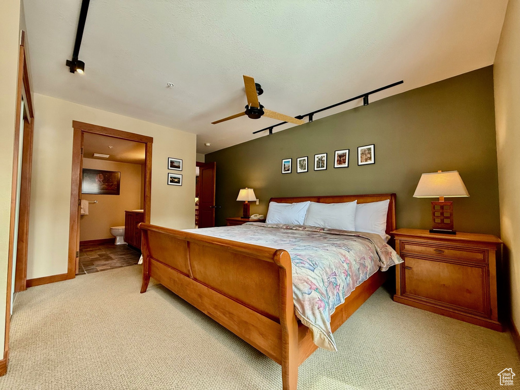 Bedroom featuring carpet flooring, baseboards, rail lighting, a ceiling fan, and ensuite bath