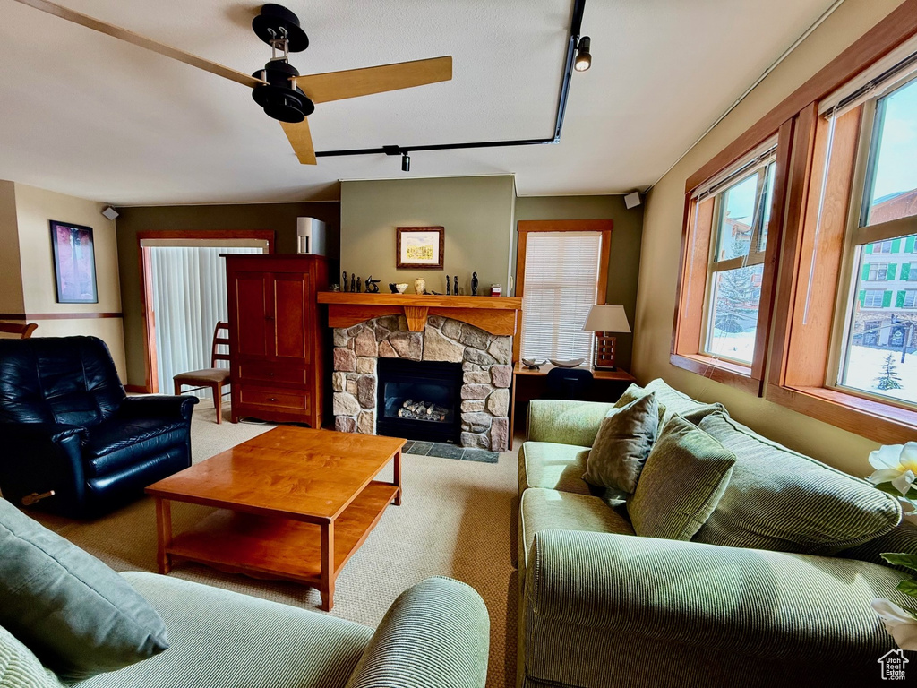 Carpeted living room featuring a ceiling fan, a stone fireplace, and rail lighting