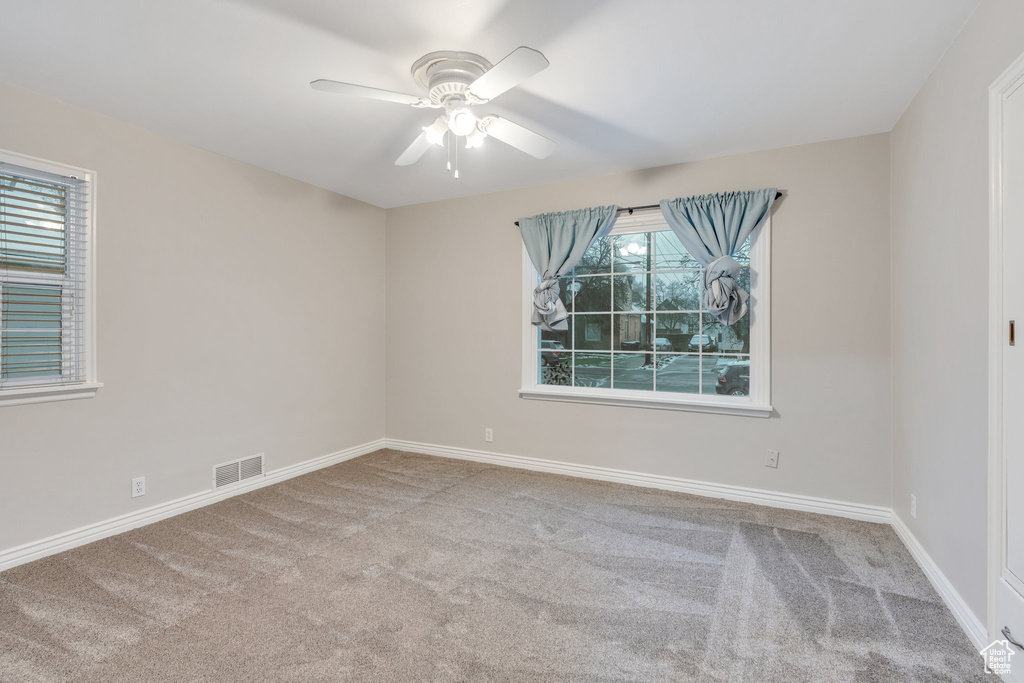 Spare room with carpet flooring, baseboards, ceiling fan, and visible vents
