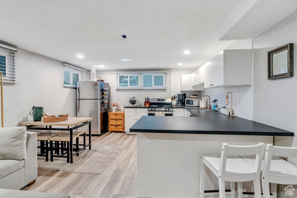 Kitchen with white cabinets, a peninsula, light wood finished floors, dark countertops, and appliances with stainless steel finishes