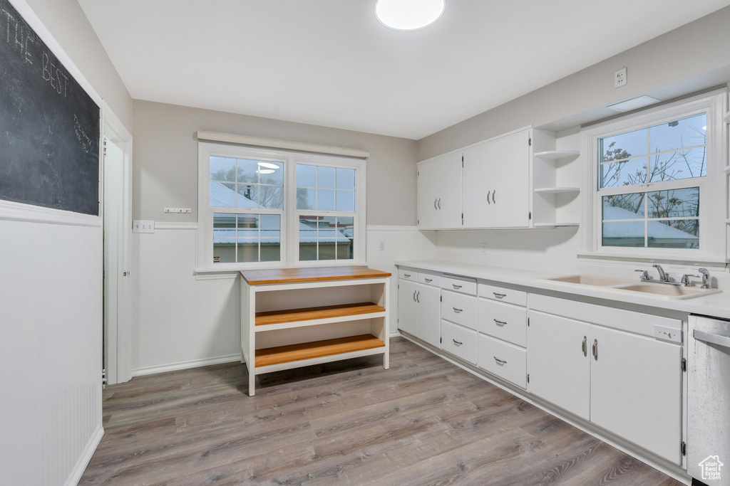 Kitchen featuring open shelves, light wood-type flooring, stainless steel dishwasher, a sink, and white cabinets
