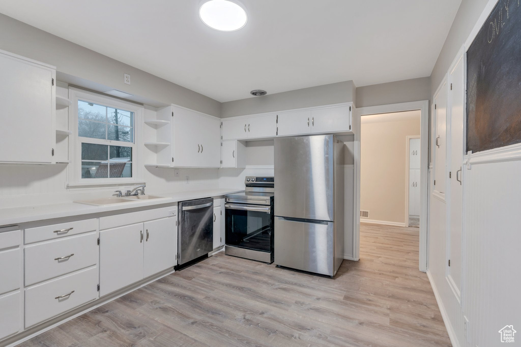 Kitchen featuring open shelves, stainless steel appliances, a sink, light wood finished floors, and white cabinets