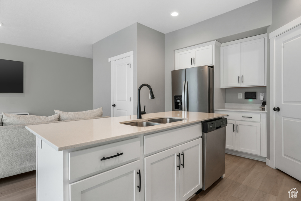 Kitchen with open floor plan, light countertops, stainless steel appliances, a sink, and light wood-style floors