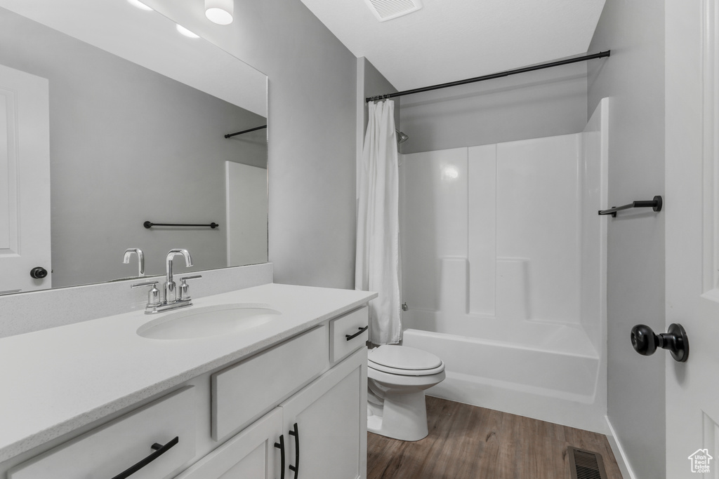 Full bathroom with toilet, vanity, wood finished floors, and visible vents