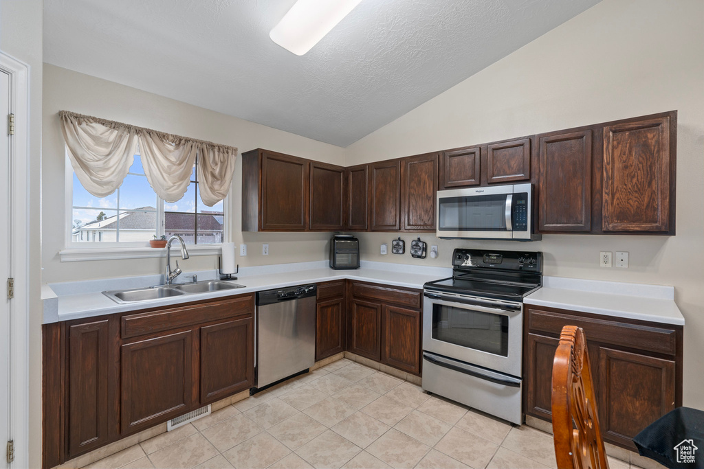Kitchen featuring a sink, vaulted ceiling, light countertops, and appliances with stainless steel finishes