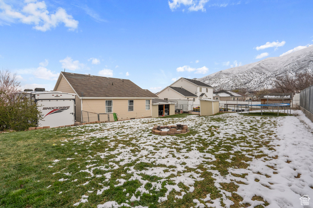 Snow covered house featuring a trampoline, a fire pit, a mountain view, and fence