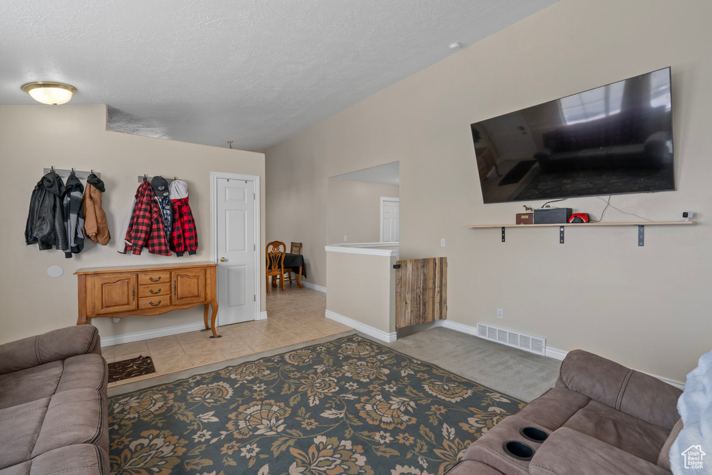 Living area featuring baseboards, visible vents, light tile patterned floors, and a textured ceiling