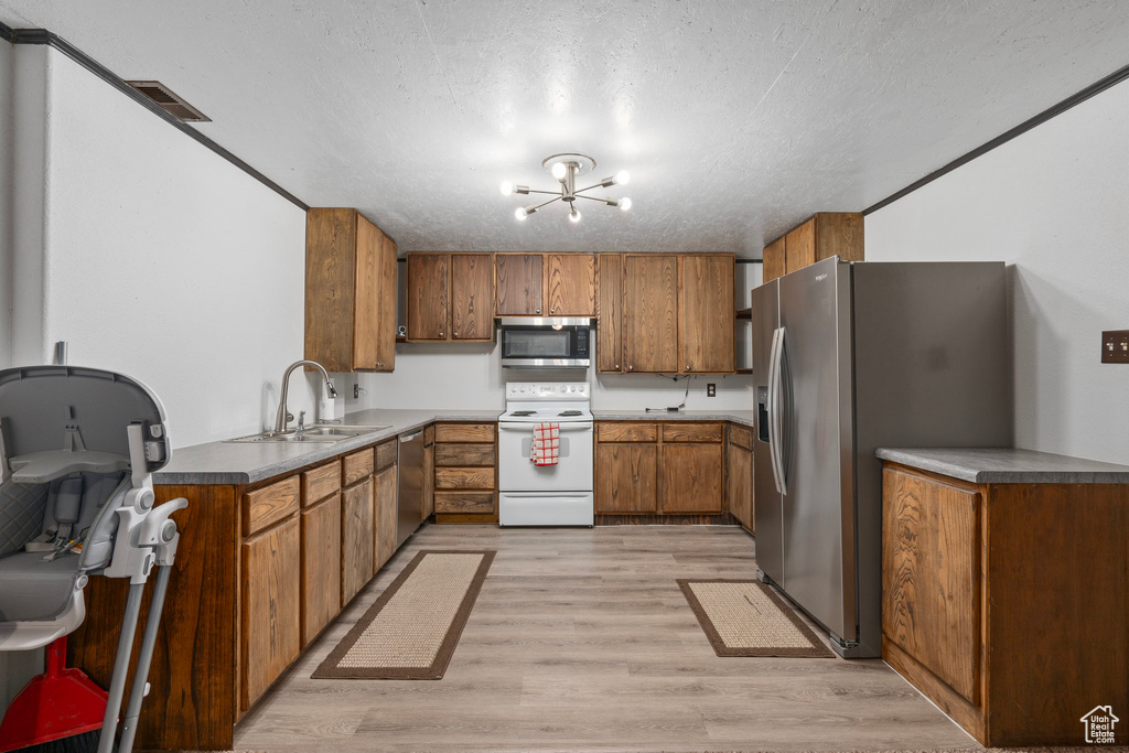 Kitchen with stainless steel appliances, a textured ceiling, a sink, light wood-style flooring, and brown cabinetry