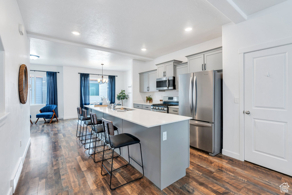 Kitchen featuring a breakfast bar area, gray cabinets, a chandelier, a center island with sink, and appliances with stainless steel finishes