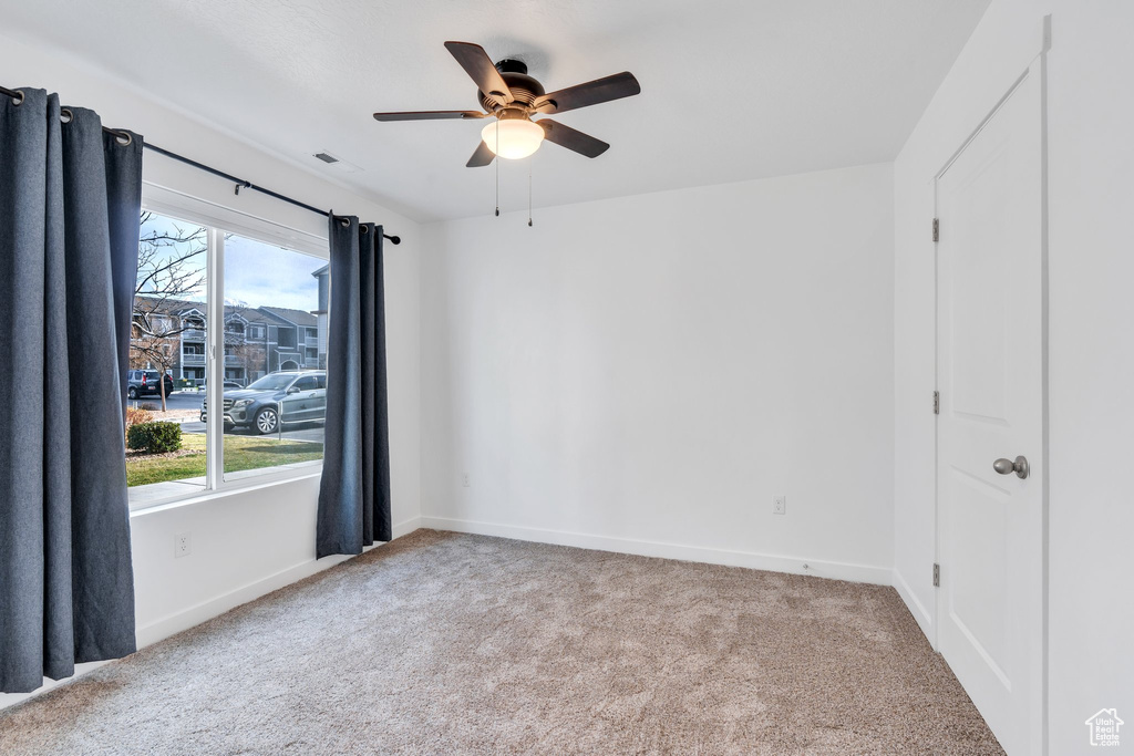 Carpeted empty room featuring plenty of natural light, baseboards, and ceiling fan