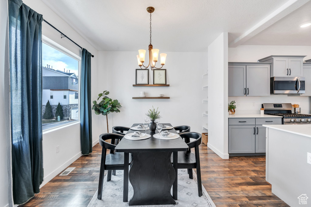 Dining room featuring dark wood-type flooring, baseboards, visible vents, and an inviting chandelier