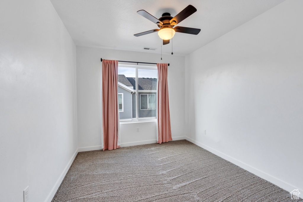 Empty room with baseboards, visible vents, ceiling fan, and carpet