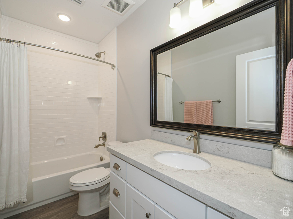 Bathroom with visible vents, toilet, wood finished floors, vanity, and shower / bathtub combination with curtain