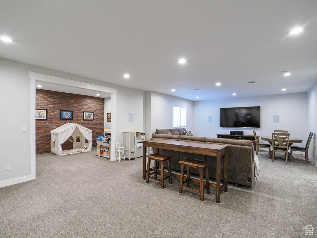 Carpeted living room featuring baseboards, recessed lighting, and brick wall