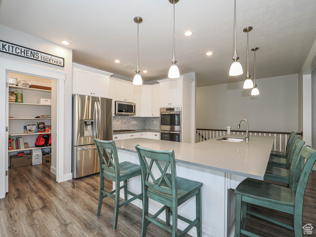 Kitchen with dark wood-style flooring, a breakfast bar, a sink, white cabinets, and appliances with stainless steel finishes