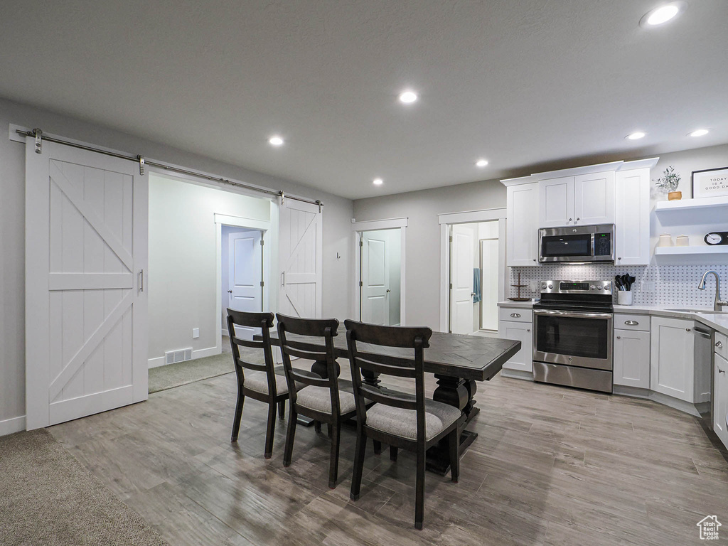 Dining room with light wood finished floors, a barn door, baseboards, visible vents, and recessed lighting