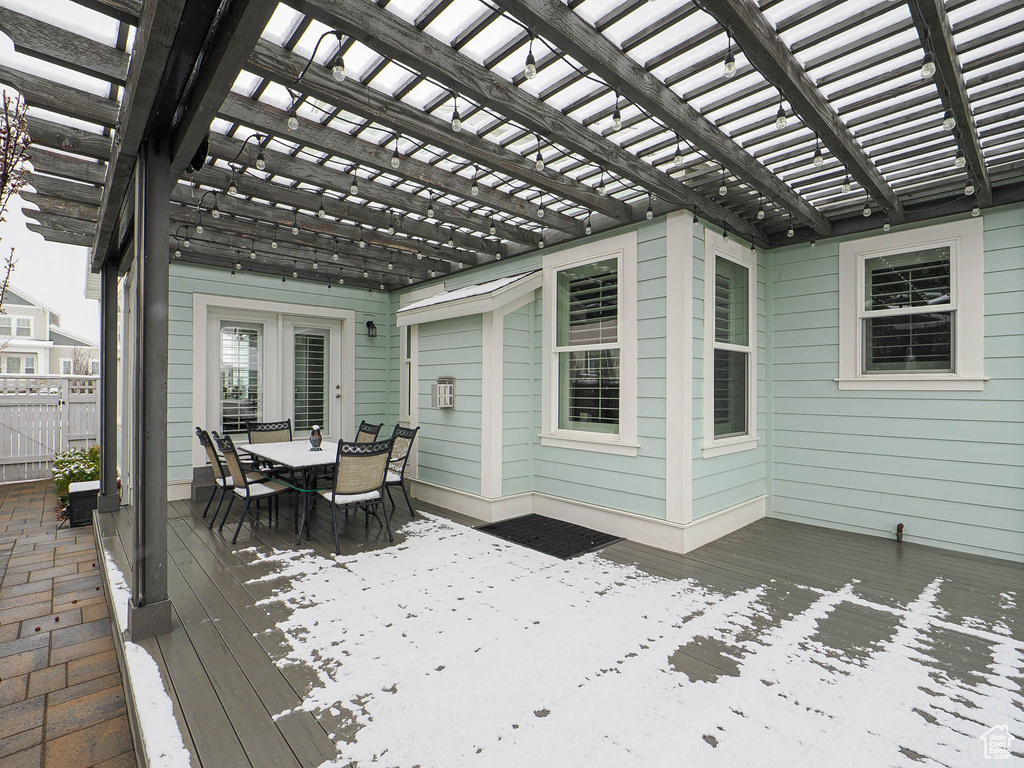 Snow covered deck featuring outdoor dining area, a pergola, and fence
