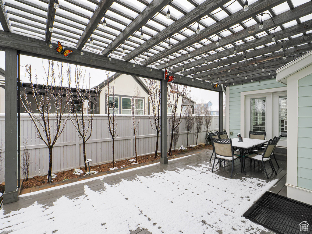 Snow covered patio featuring a pergola, outdoor dining area, and fence