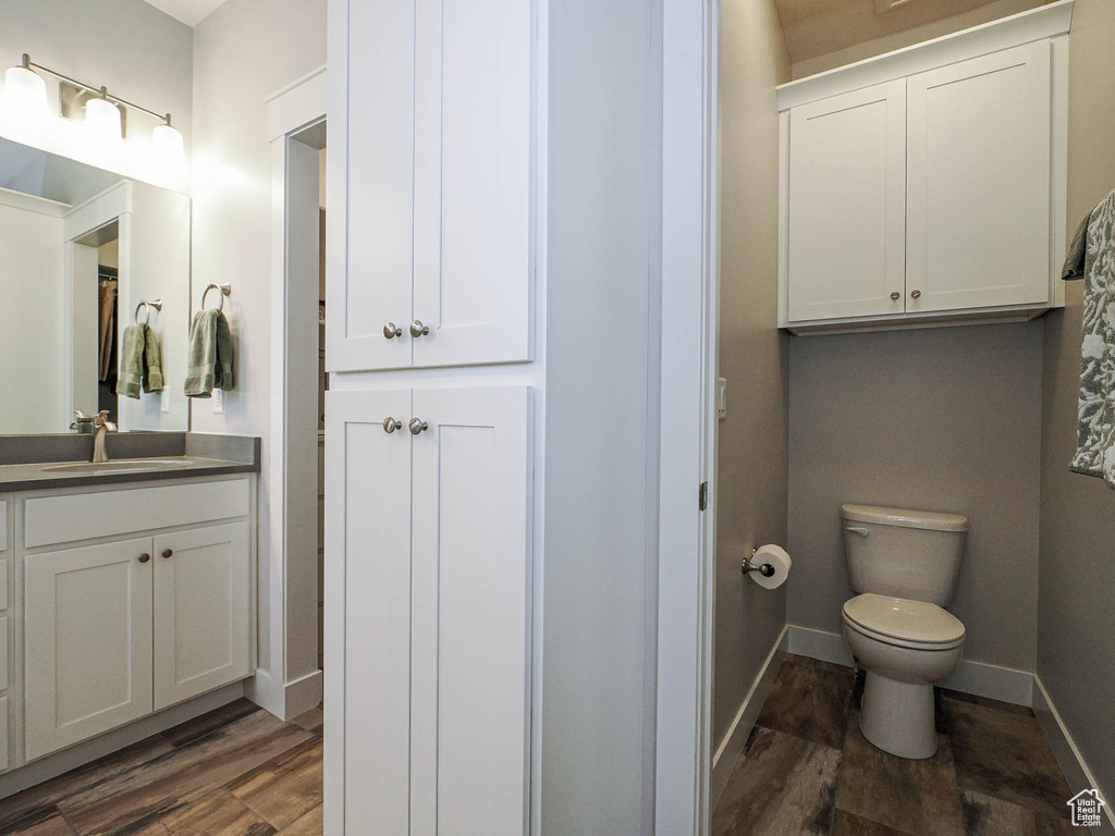 Bathroom featuring baseboards, toilet, wood finished floors, and vanity