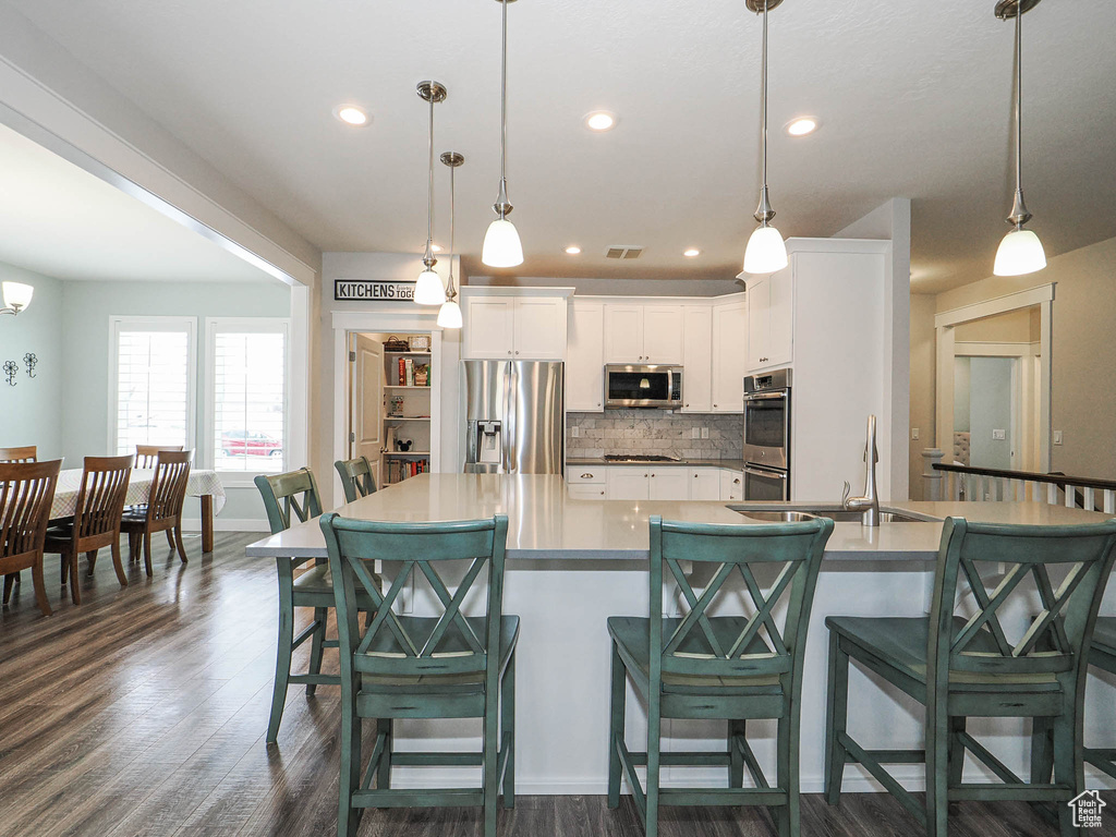Kitchen with a sink, white cabinetry, tasteful backsplash, appliances with stainless steel finishes, and dark wood-type flooring