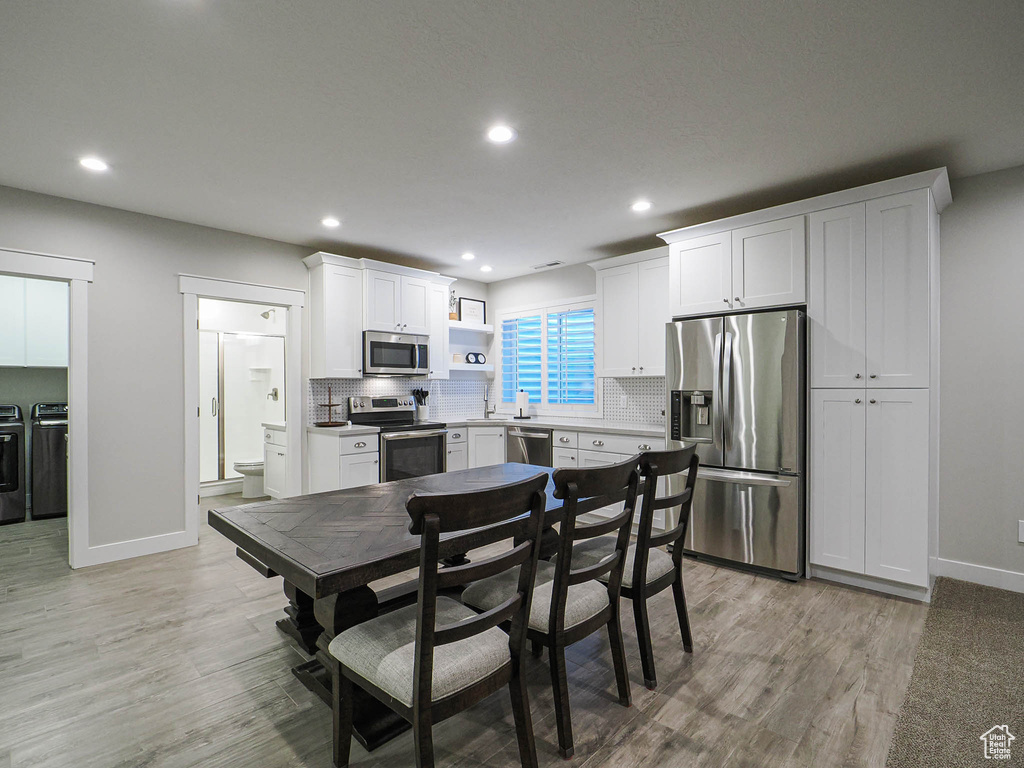 Kitchen featuring backsplash, open shelves, white cabinetry, separate washer and dryer, and stainless steel appliances