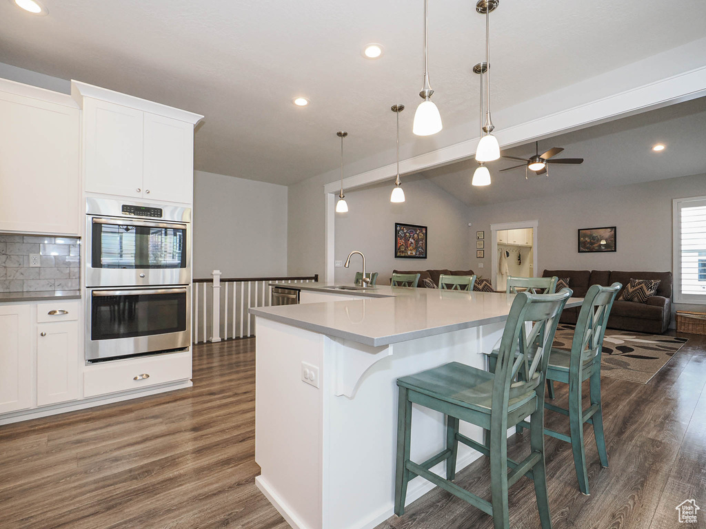 Kitchen with open floor plan, stainless steel double oven, vaulted ceiling with beams, and dark wood finished floors