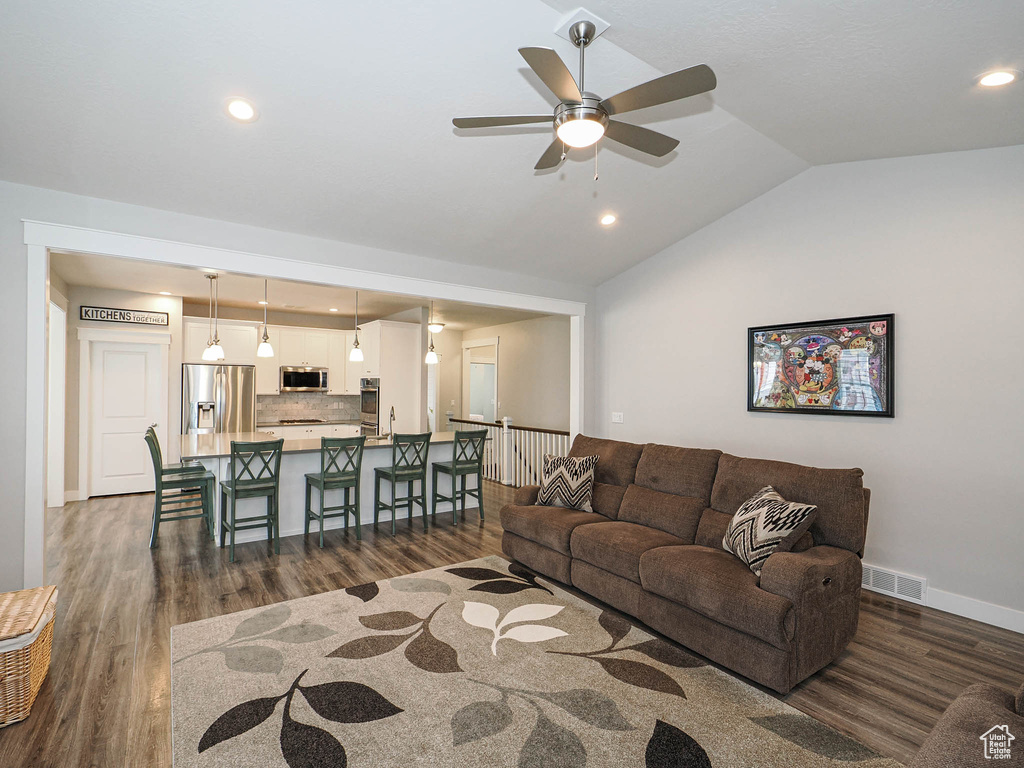 Living room featuring vaulted ceiling, baseboards, dark wood-style floors, visible vents, and a ceiling fan