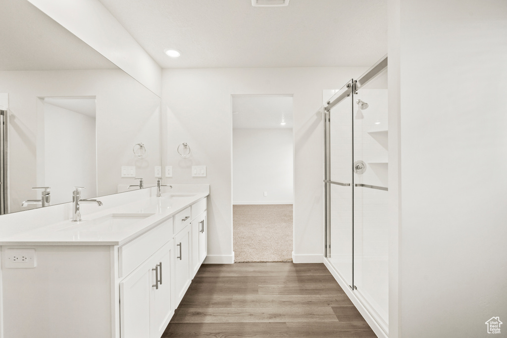 Full bathroom with double vanity, a shower stall, a sink, and wood finished floors