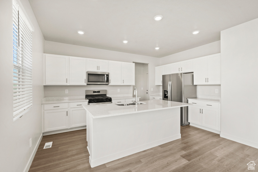 Kitchen featuring white cabinets, a sink, light wood finished floors, light countertops, and stainless steel appliances