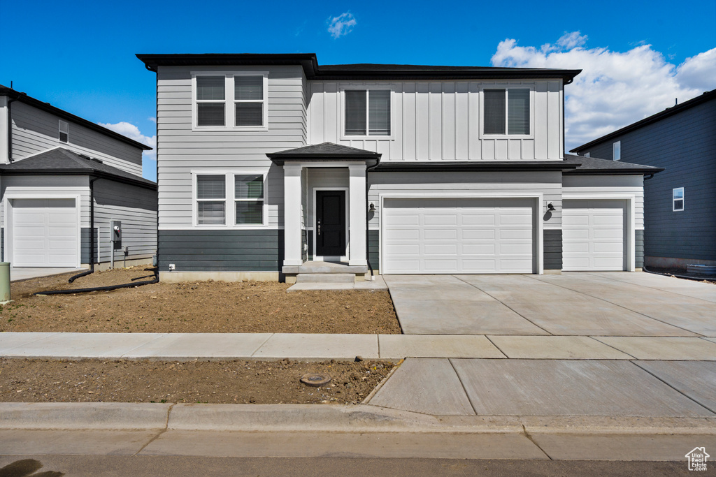 View of front of property with board and batten siding, an attached garage, and driveway