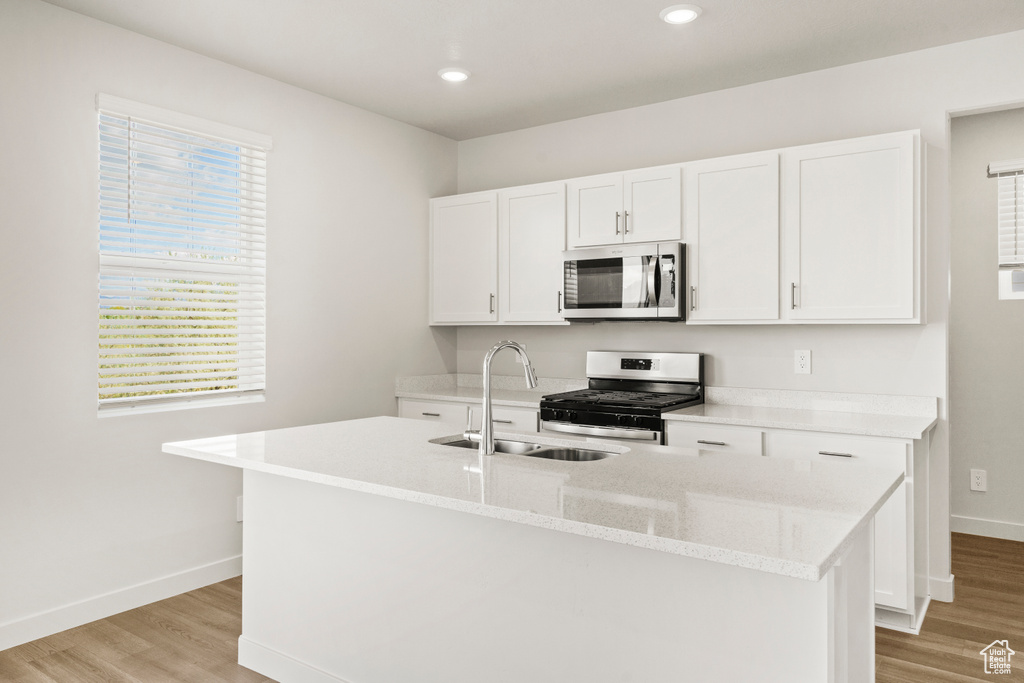 Kitchen featuring baseboards, light wood-type flooring, white cabinetry, a sink, and appliances with stainless steel finishes