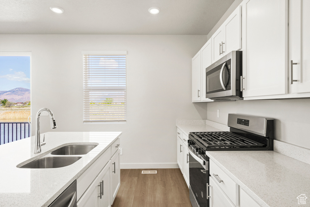 Kitchen with visible vents, appliances with stainless steel finishes, wood finished floors, a sink, and baseboards