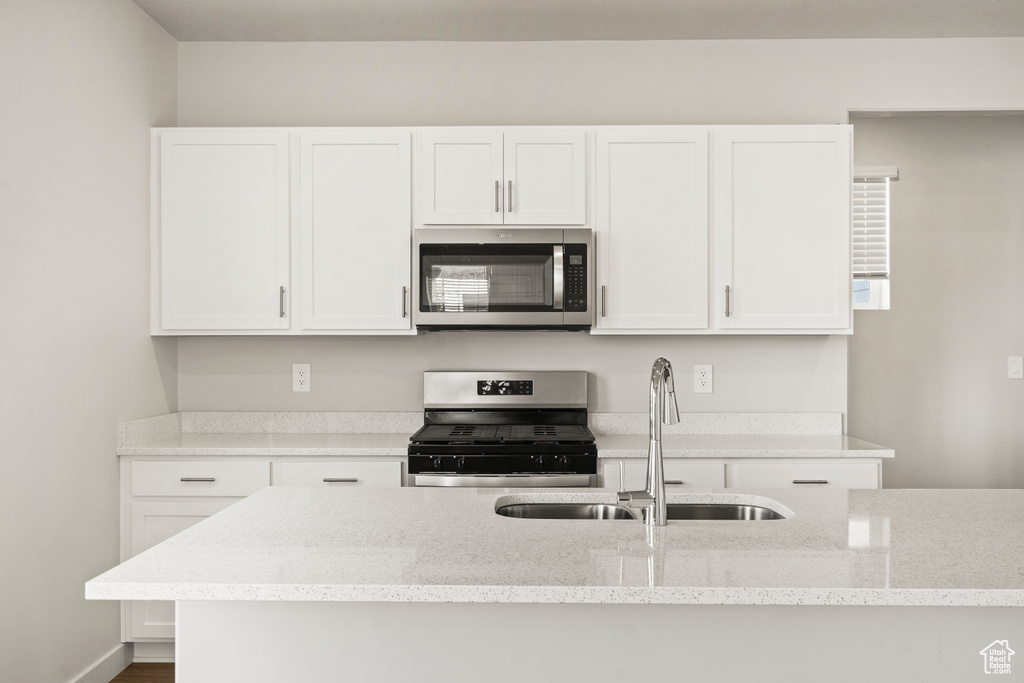 Kitchen with white cabinets, appliances with stainless steel finishes, a sink, and light stone counters