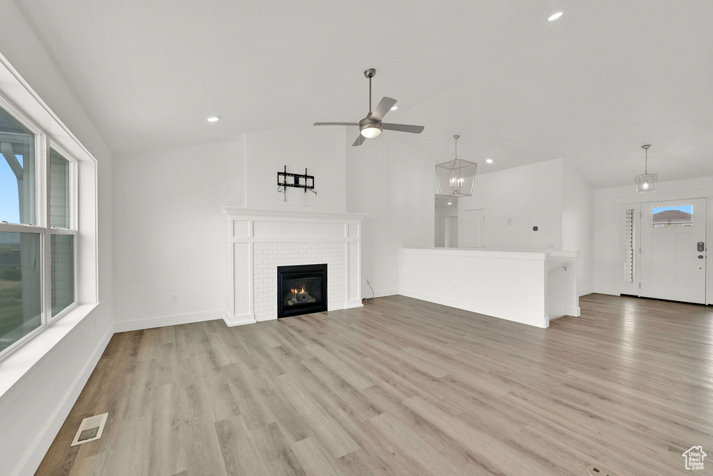 Unfurnished living room featuring ceiling fan, lofted ceiling, light wood-style flooring, plenty of natural light, and a glass covered fireplace