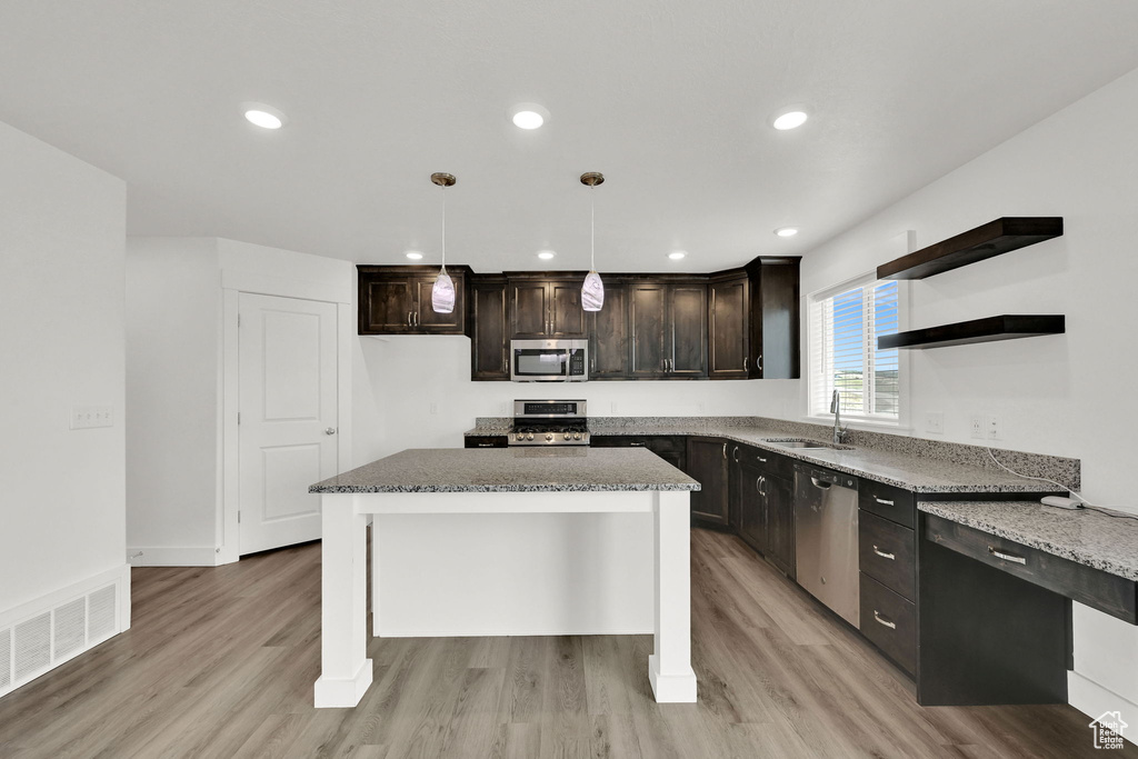 Kitchen featuring appliances with stainless steel finishes, light stone countertops, light wood finished floors, dark brown cabinets, and recessed lighting