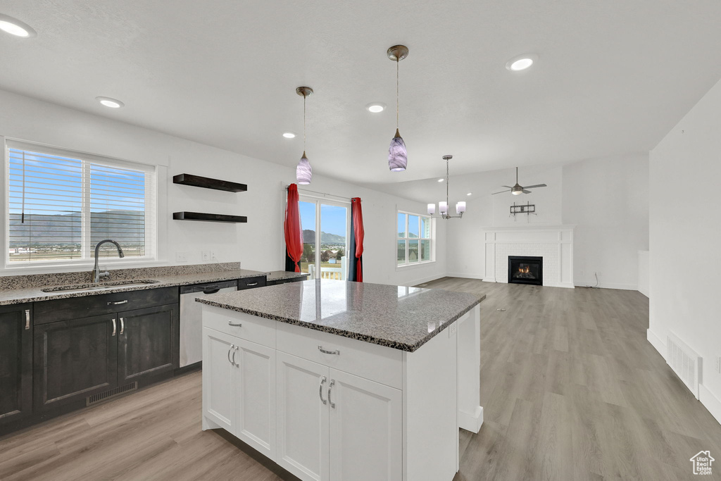 Kitchen featuring stainless steel dishwasher, a glass covered fireplace, light wood-type flooring, a center island, and dark stone counters