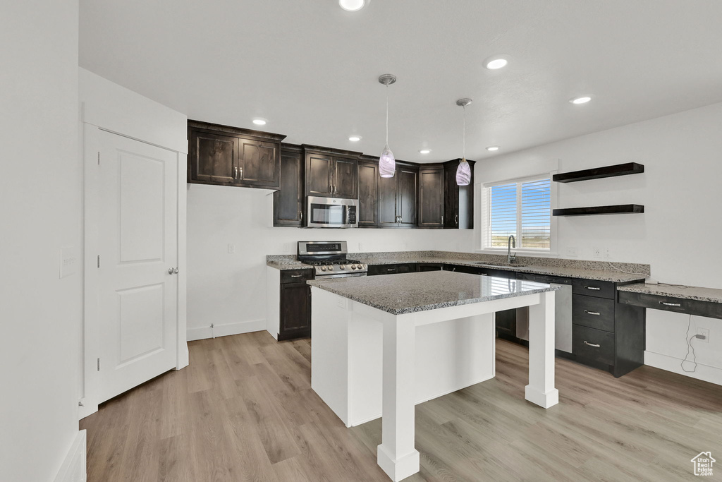 Kitchen with appliances with stainless steel finishes, stone counters, light wood-style flooring, dark brown cabinets, and a kitchen island