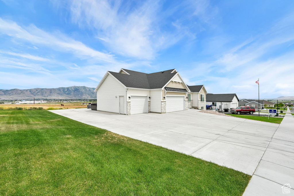View of property exterior featuring a yard, a mountain view, driveway, and a garage