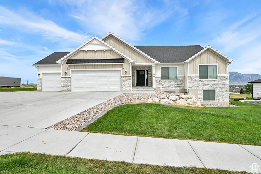 Craftsman house with board and batten siding, stone siding, an attached garage, a front yard, and driveway