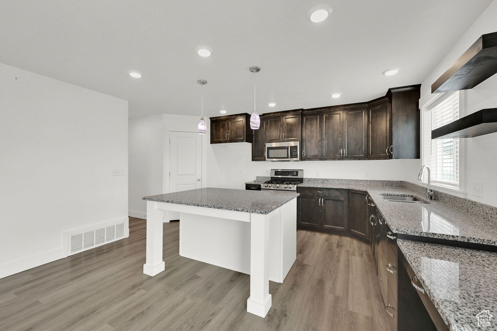 Kitchen featuring stainless steel appliances, dark brown cabinetry, stone countertops, light wood-type flooring, and recessed lighting