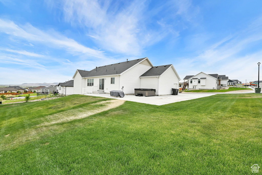 Back of property featuring a hot tub, a patio, a lawn, and a residential view