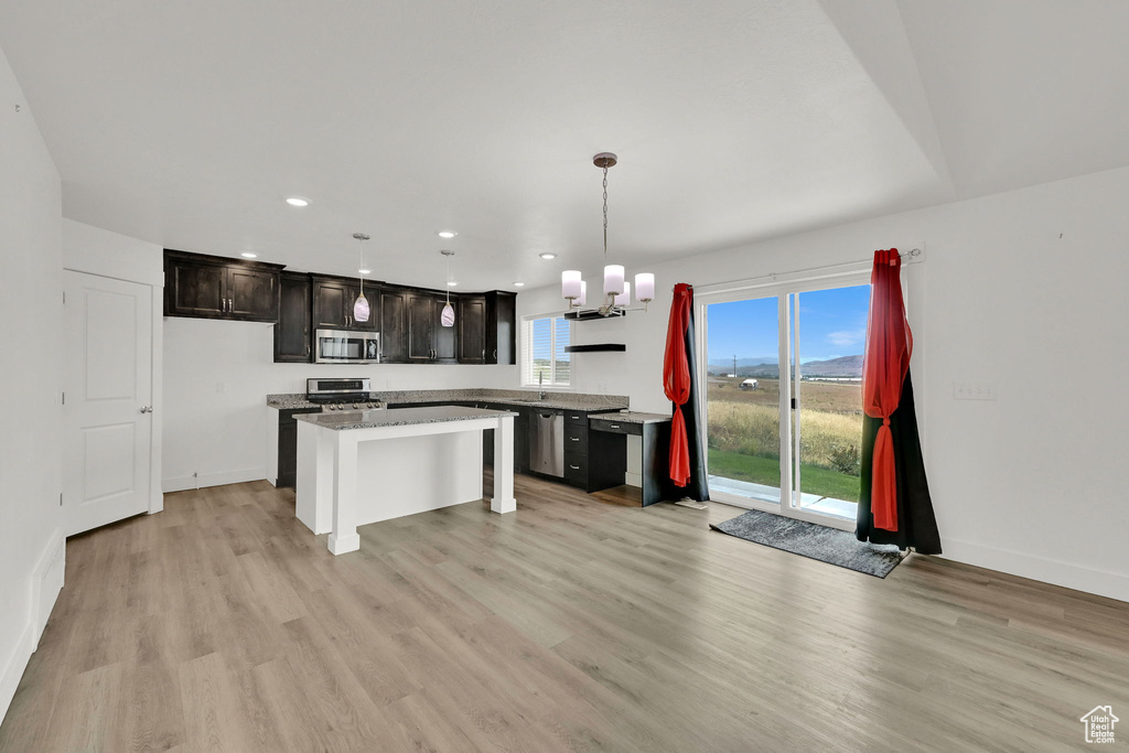 Kitchen with appliances with stainless steel finishes, light wood-style floors, a chandelier, a center island, and decorative light fixtures