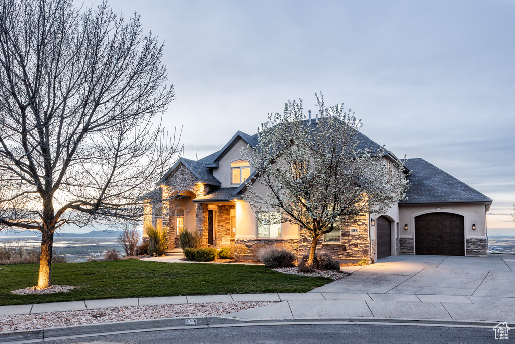 French country home with a garage, concrete driveway, stone siding, and a front lawn