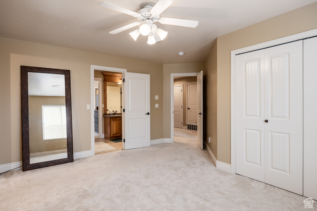 Unfurnished bedroom with a closet, light carpet, ensuite bathroom, baseboards, and ceiling fan