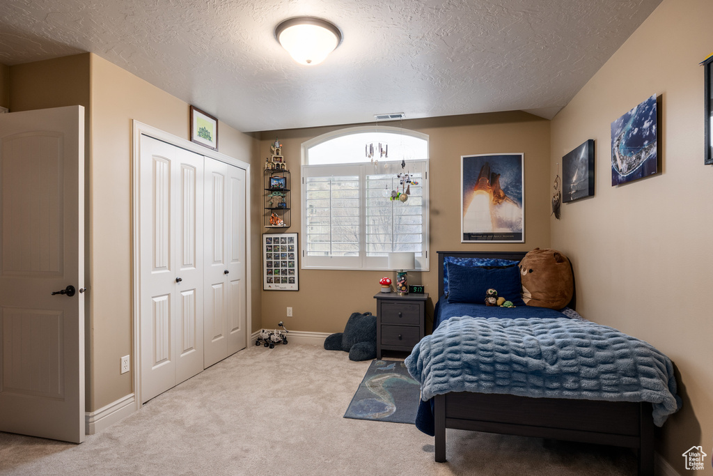 Carpeted bedroom featuring baseboards, a textured ceiling, a closet, and visible vents