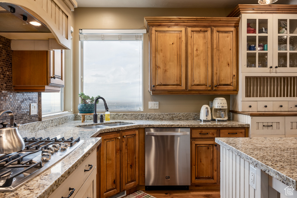 Kitchen with a sink, appliances with stainless steel finishes, light stone counters, and brown cabinets