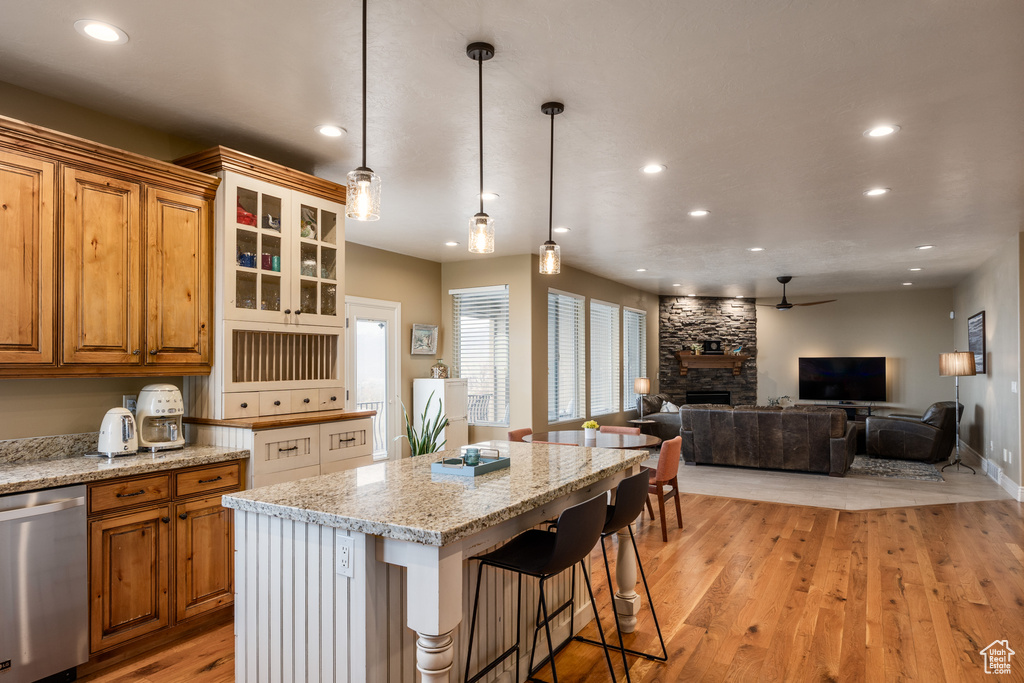 Kitchen with light wood finished floors, brown cabinetry, a fireplace, and stainless steel dishwasher