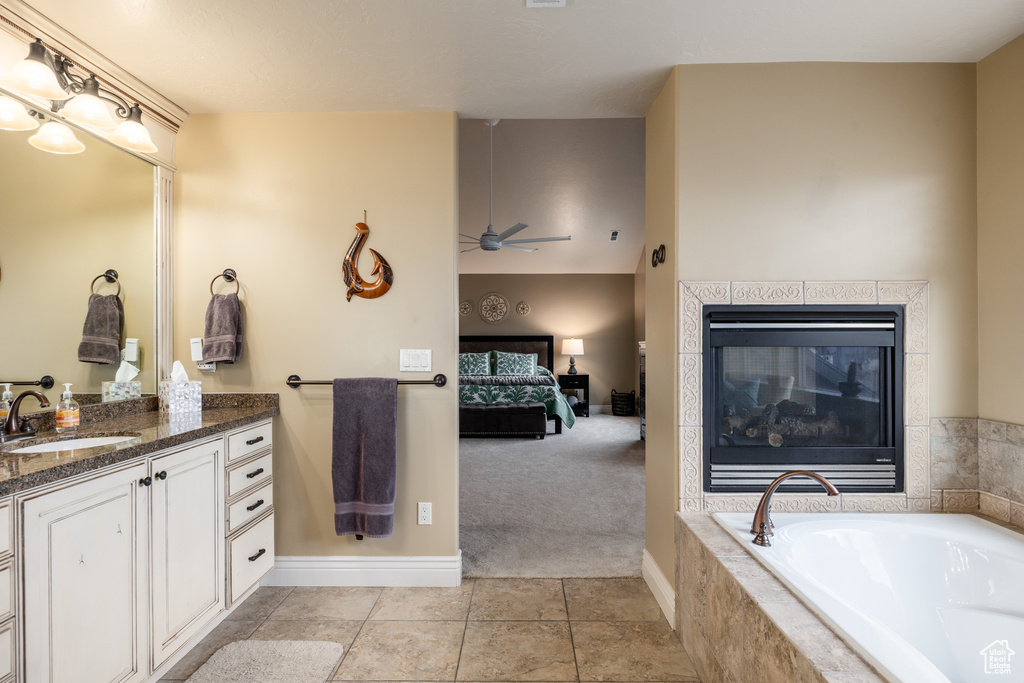 Ensuite bathroom featuring vanity, ensuite bath, a ceiling fan, a fireplace, and a bath