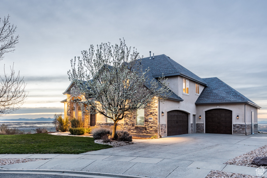 French country home with driveway, stucco siding, stone siding, and an attached garage