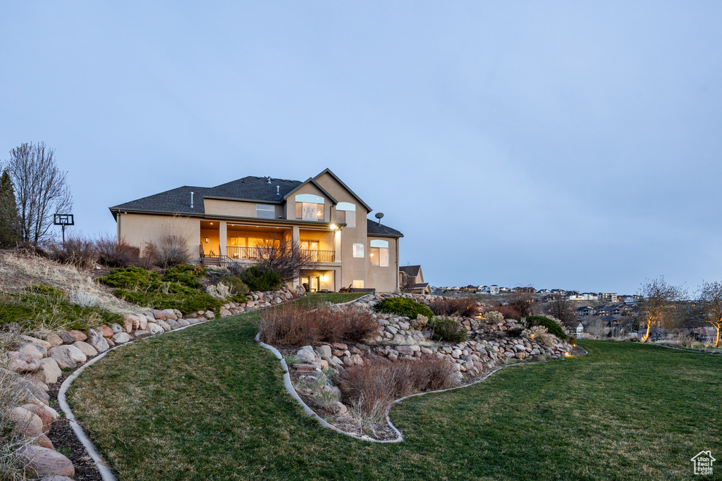 Back of house with a balcony, stucco siding, and a lawn